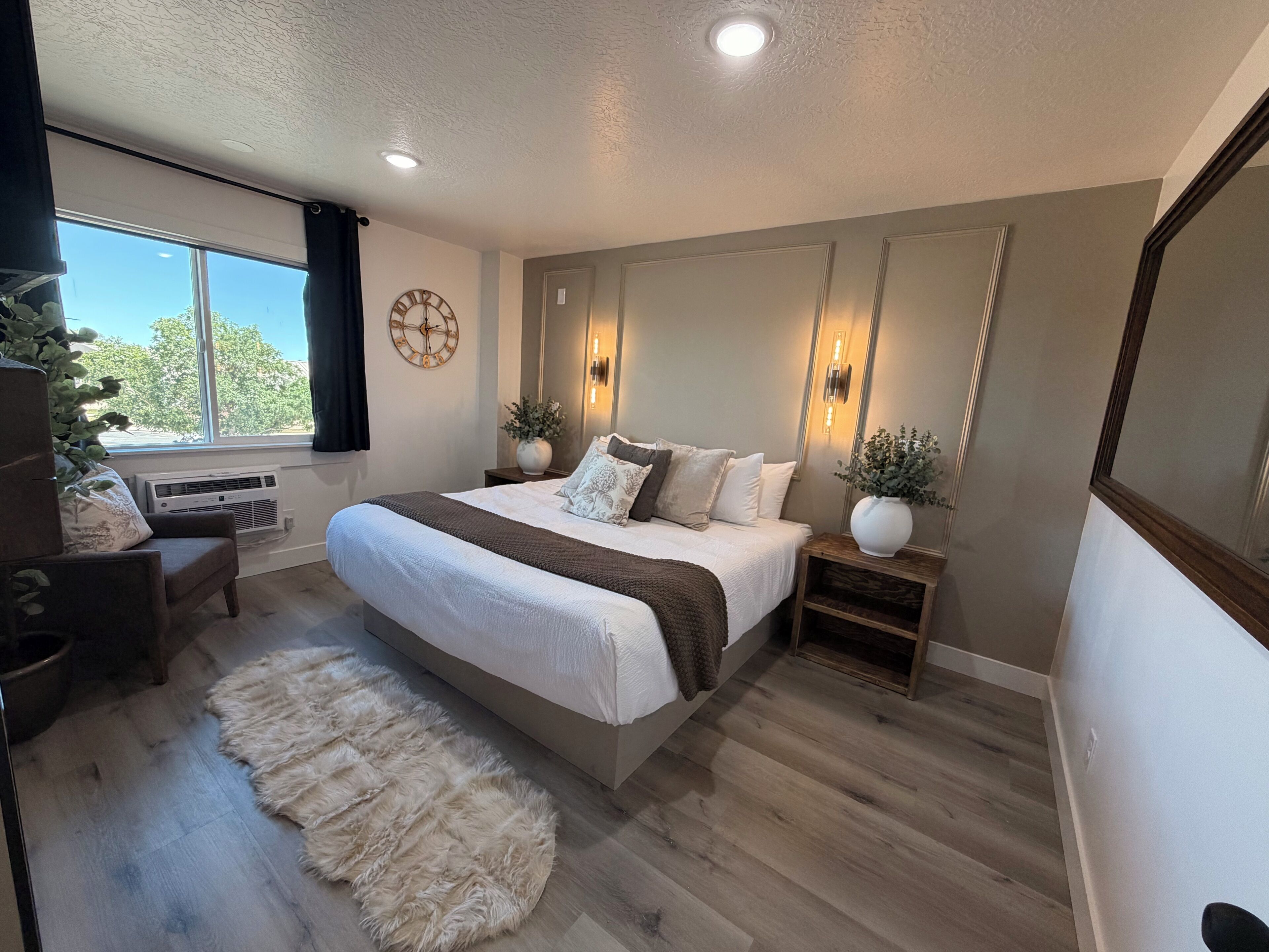 A bedroom with a large bed, bedside tables, a window, and a view of trees.
