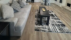 A spacious living room with a gray sofa, a coffee table, and a patterned rug. - CB&M Downtown Suites (Roosevelt)