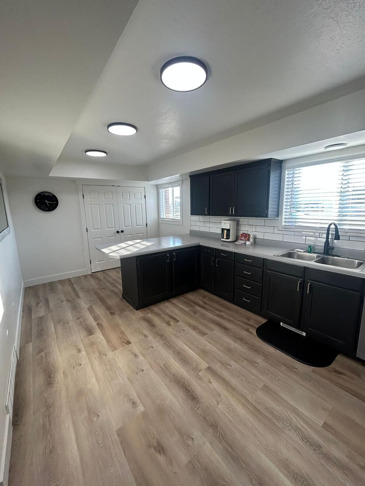A modern kitchen with dark cabinets, a white countertop, and a wooden floor.