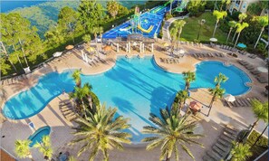 A large outdoor swimming pool with multiple sections, surrounded by palm trees and lounge areas. - 5BR Disney Villa | Pool, Spa & Game Room (Kissimmee)