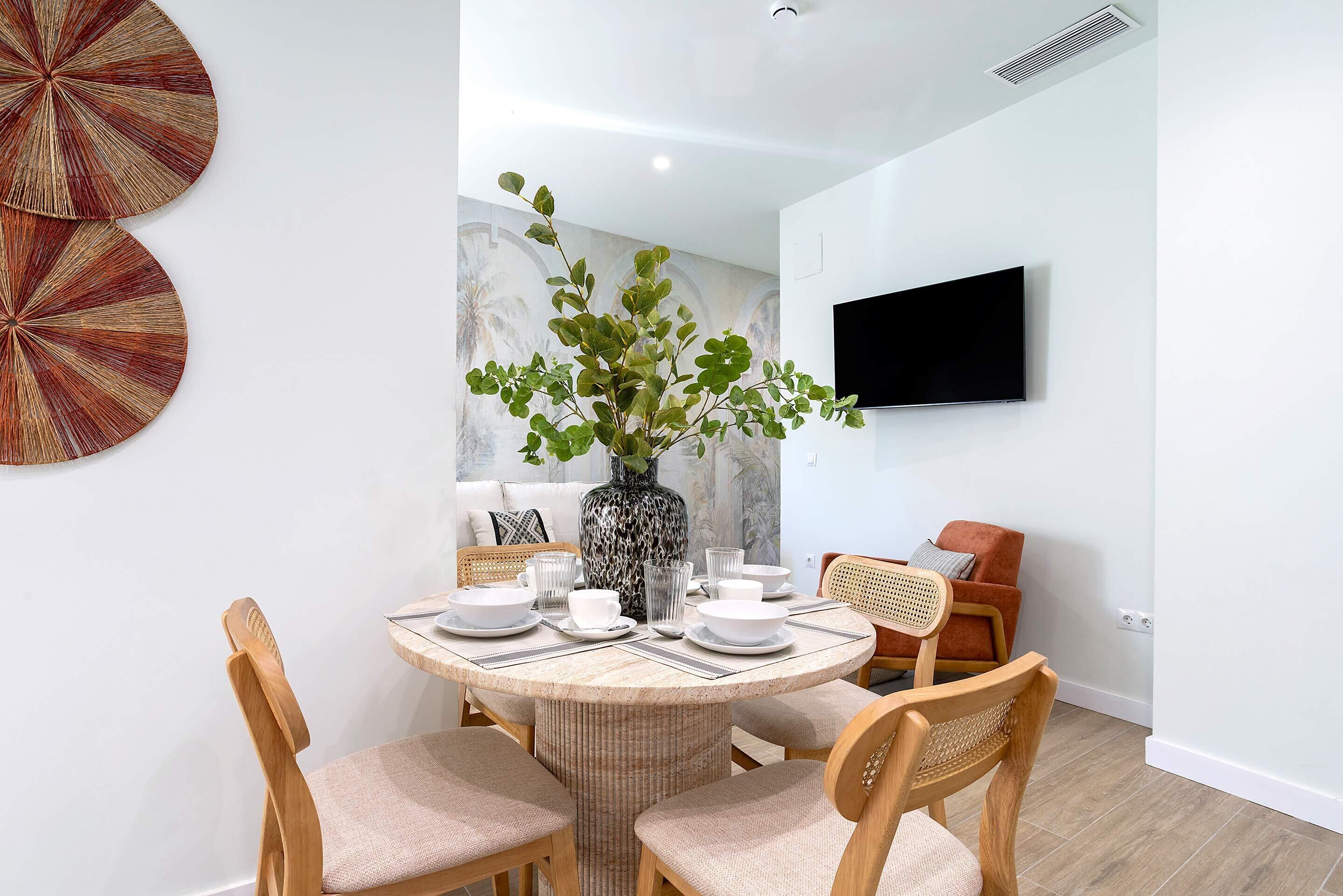 Een eetgedeelte met een ronde tafel, stoelen en een vaas met groene planten.