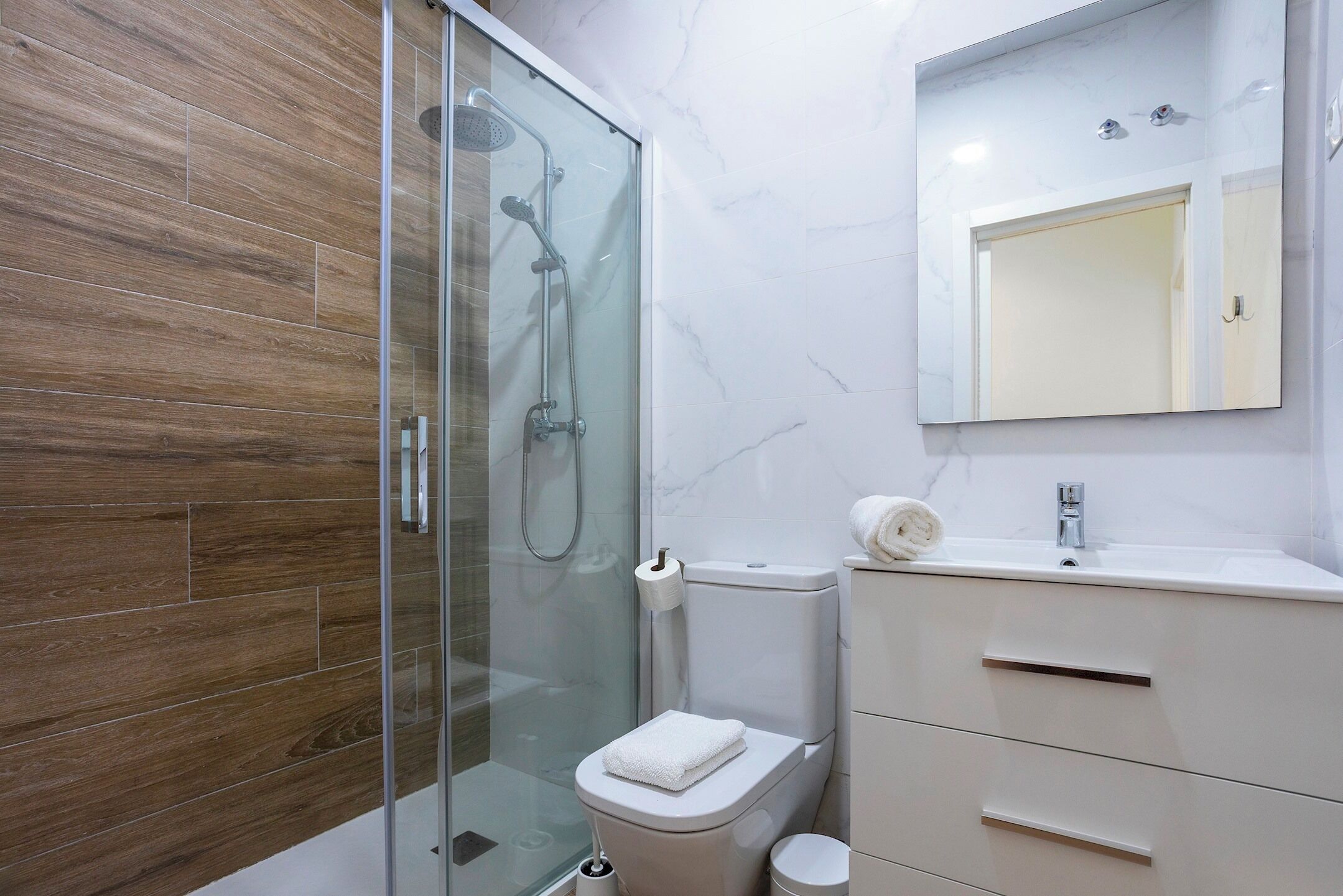 A modern bathroom with a glass-enclosed shower, a toilet, and a vanity with a mirror.
