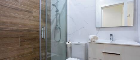 A modern bathroom with a glass-enclosed shower, a toilet, and a vanity with a mirror.