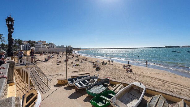 Una playa con barcos, gente y un cielo despejado.