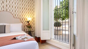 Habitación de hotel con cama, mesita de noche, lámpara y vistas al exterior.