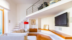 Una sala de estar moderna con un sofá blanco, una lámpara roja y un televisor grande en la pared.