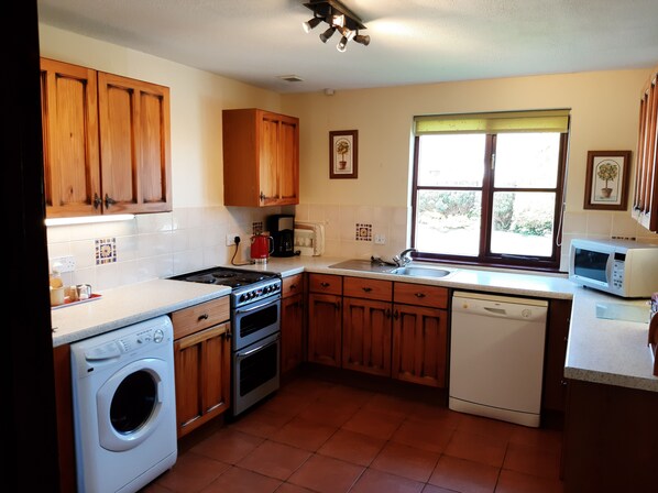 A compact kitchen with wooden cabinets, a washing machine, a stove, and a dishwasher. - Large, Comfortable, Family/Group Cottage, Hot Tub, Dog Friendly, Seasonal Heated Outdoor Pool. (Cardigan)