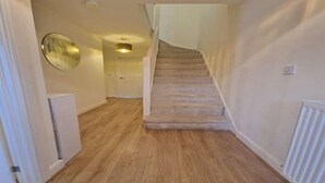 Ein Flur mit Teppichboden, einer weißen Tür, einem Spiegel und einer Treppe.