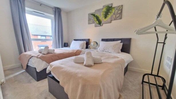 Ein Hotelzimmer mit zwei Betten, einer Hängelampe, einem Wandbild und einem Kleiderständer.