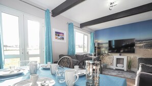 A dining area with a table set for four, a television mounted on the wall, and a scenic mural. - Family Friendly, Dog Friendly Cottage, Seasonal Outdoor Heated Pool, FootGolf Course, Games Field. (Cardigan)