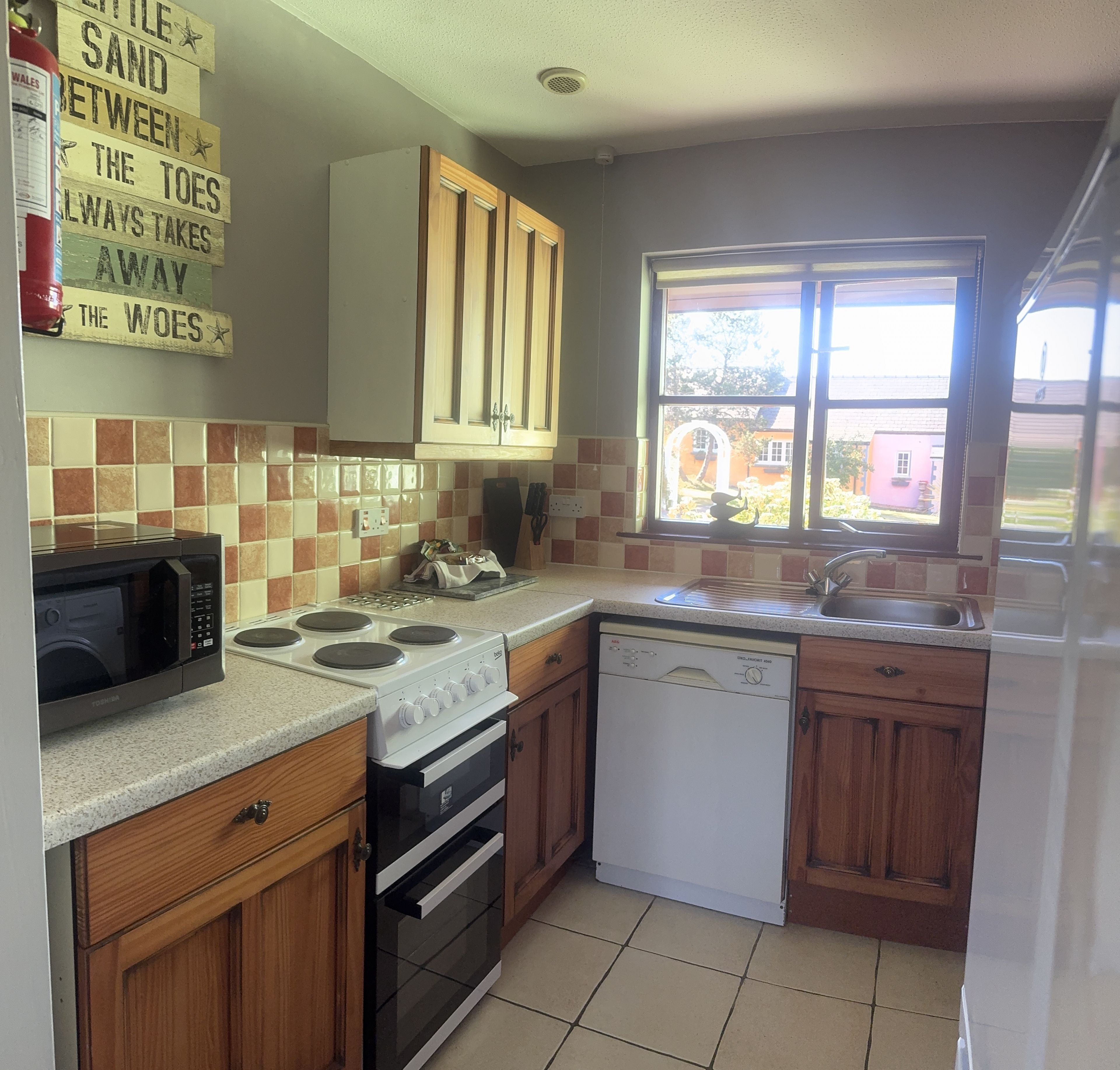 Cocina equipada con microondas, estufa, horno y lavavajillas. Hay una ventana con vista a una casa y un cartel en la pared.