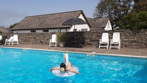 A swimming pool with clear blue water, surrounded by white lounge chairs and a stone wall.