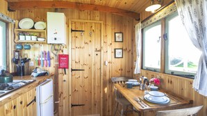 A wooden cabin kitchen with a dining table, chairs, and a window with curtains.