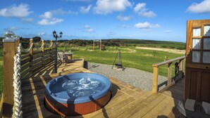 A wooden deck with a hot tub, a swing, and a view of the countryside.