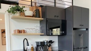 Una cuina moderna amb armaris grisos, un frigorífic d'acer inoxidable, una cafetera i un rentaplat.