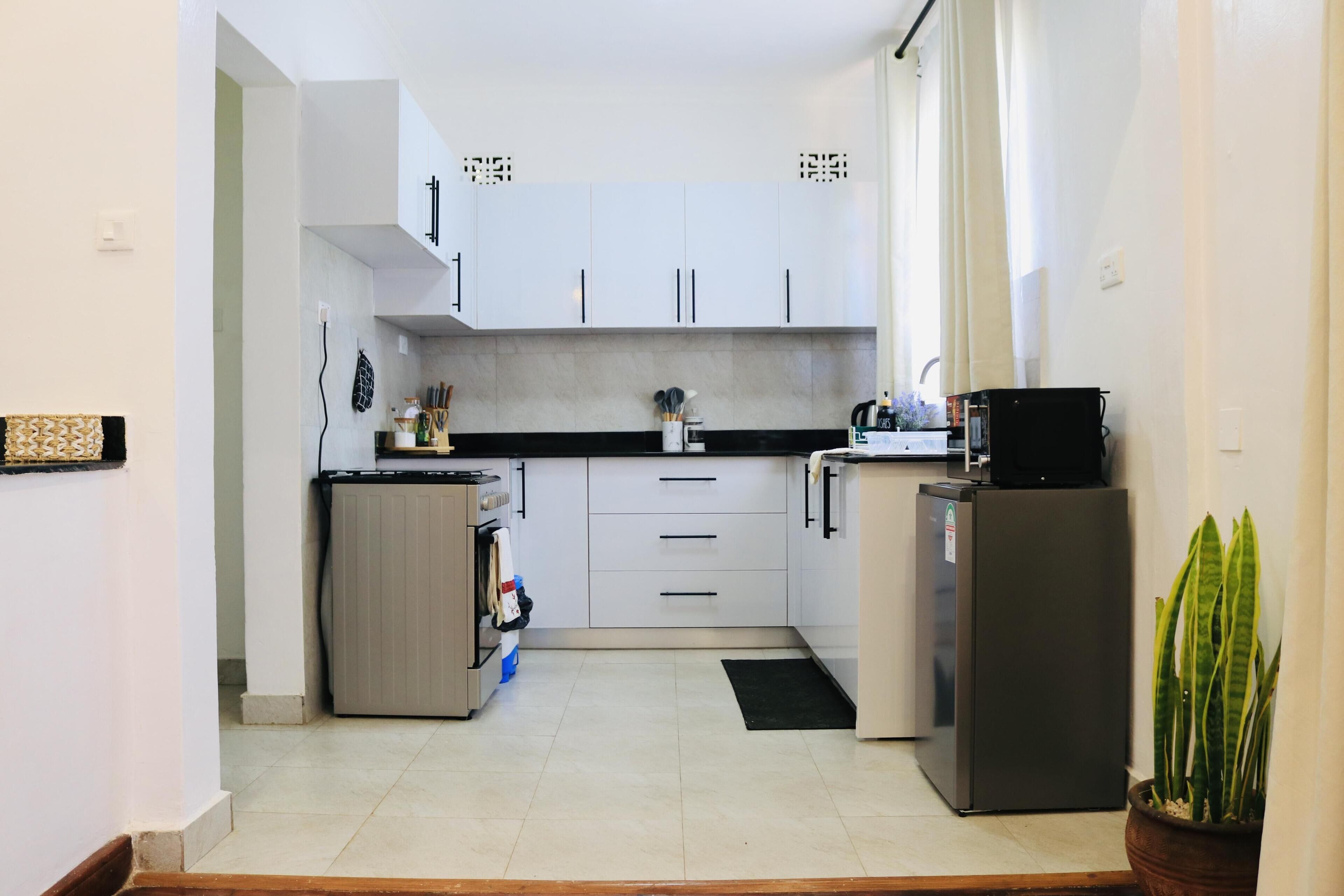 A compact kitchen with white cabinets, a built-in oven, a refrigerator, and a potted plant.