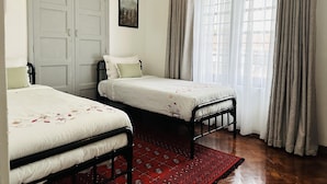 A bedroom with two single beds, a red patterned rug, a white door, and a window with sheer curtains. - Farmhouse Retreat on 85-acre tea Estate - 2331 (Limuru)
