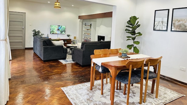A modern living room with a sofa, a dining table with chairs, a TV, and a fireplace. - Farmhouse Retreat on 85-acre tea Estate - 2331 (Limuru)