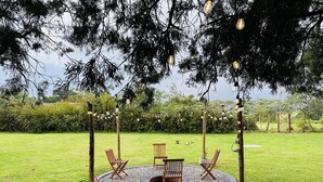 An outdoor seating area with a circular arrangement of chairs and tables, surrounded by a gravel circle, under a tree with hanging lights. - Farmhouse Retreat on 85-acre tea Estate - 2331 (Limuru)