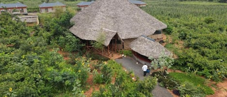 Una estructura con techo de paja y un espacio central abierto, rodeada de vegetación exuberante y otras construcciones similares al fondo.