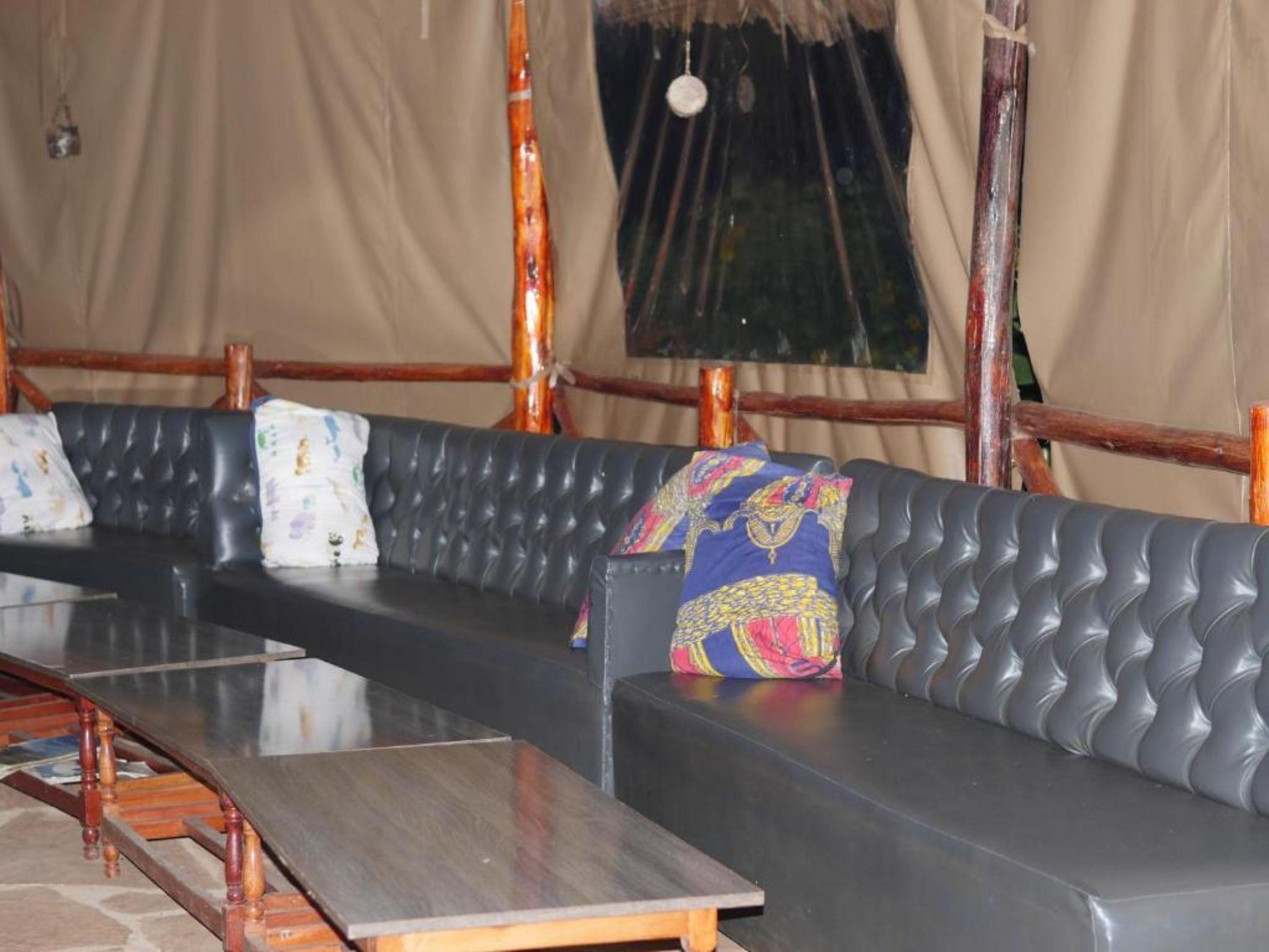 Un long banc rembourré, avec une table en bois devant, placé devant une zone couverte par une tente et soutenue par des poutres en bois.