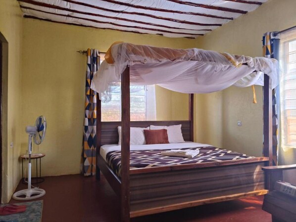 Una cama con dosel, un ventilador de pie y un tapete estampado.