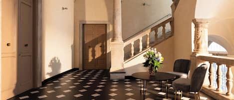 A lobby with a checkered floor, a staircase, and a seating area with a table and chairs.
