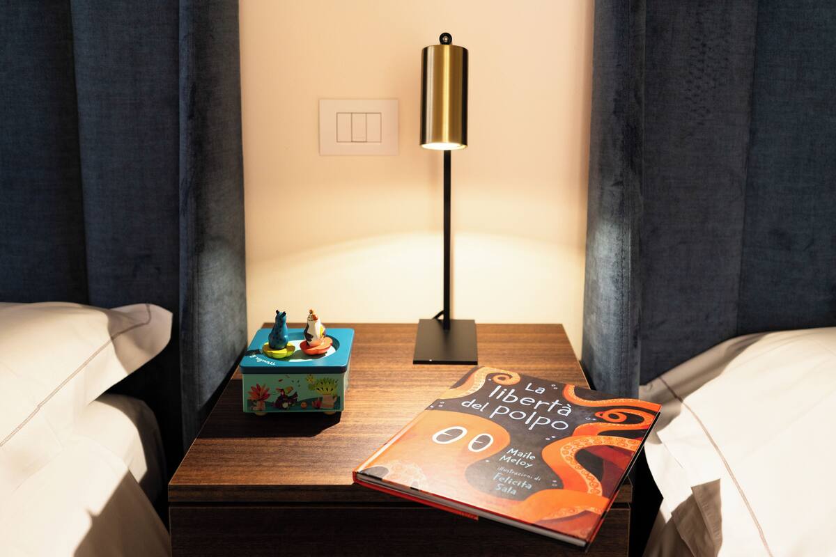 A neatly made hotel room with a wooden nightstand, a lamp, a book, and a decorative box.