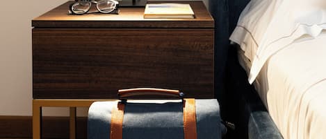 A neatly made bed with a blue headboard, a bedside table with a lamp, a small clock, and a suitcase on the floor.