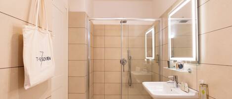 A modern bathroom with a glass-enclosed shower, a white sink, and a large mirror. A white towel hangs on the wall.