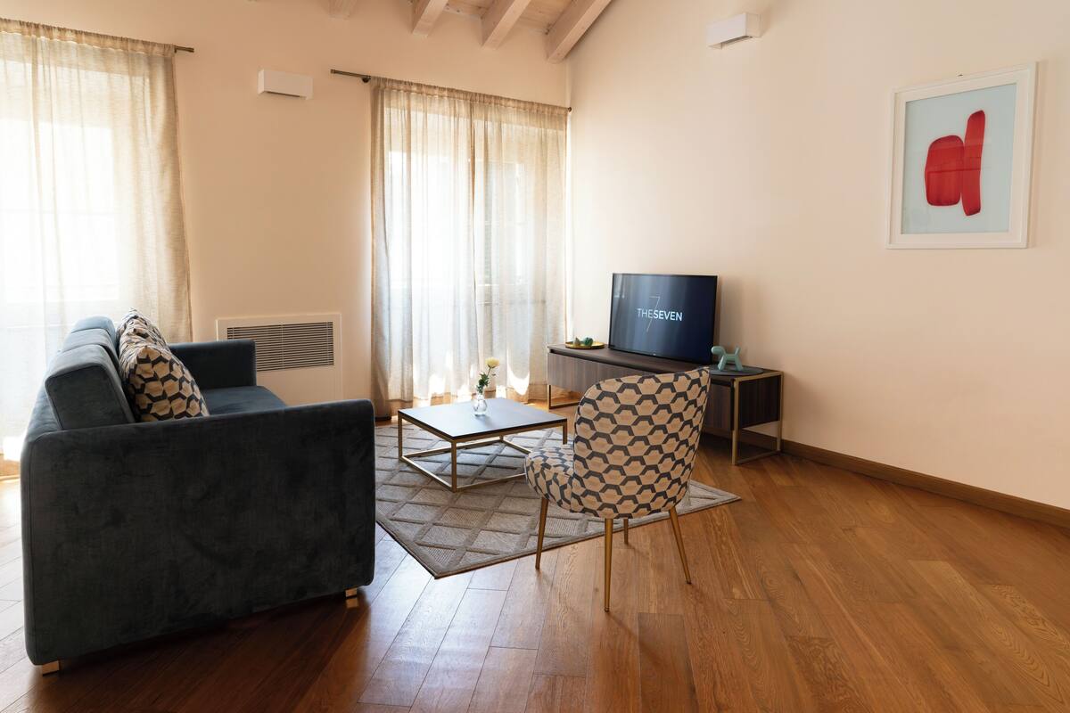 A living room with a sofa, a patterned armchair, a coffee table, and a television on a stand.