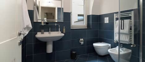 A modern bathroom with a sink, toilet, bidet, and a glass shower enclosure.