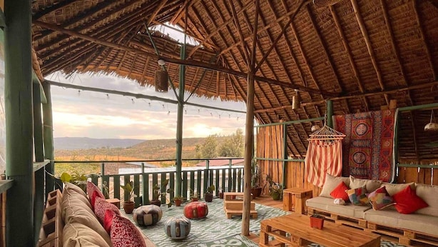 A cozy outdoor seating area with a thatched roof, wooden furniture, and a view of the landscape.