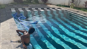 A swimming pool with clear water, surrounded by a tiled deck and a white wall.