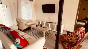 A living room with a white sofa, a patterned armchair, a coffee table, and a TV mounted on the wall.