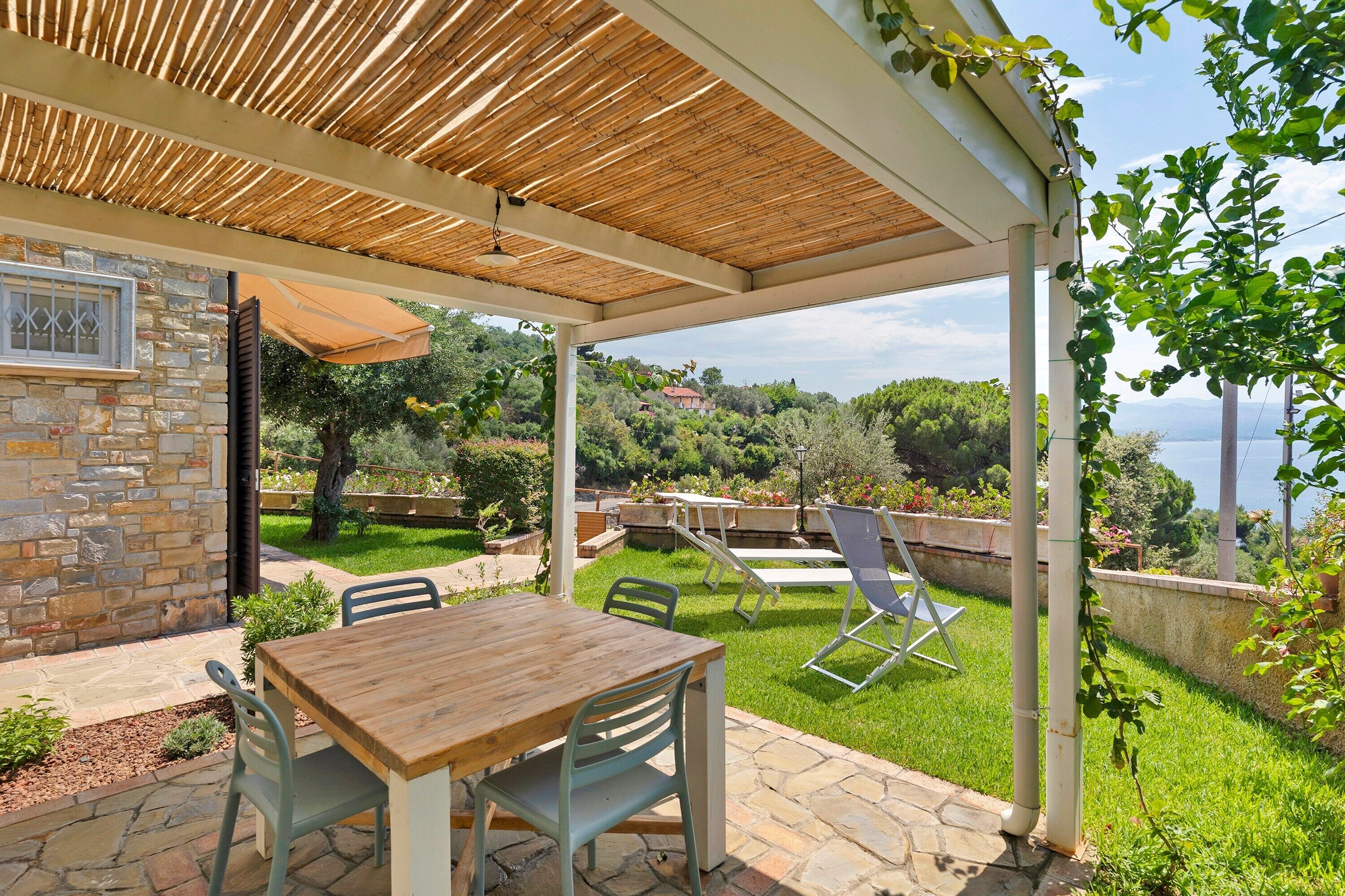 A covered patio with a stone wall, a wooden table, and chairs.