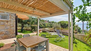 A covered patio with a stone wall, a wooden table, and chairs.