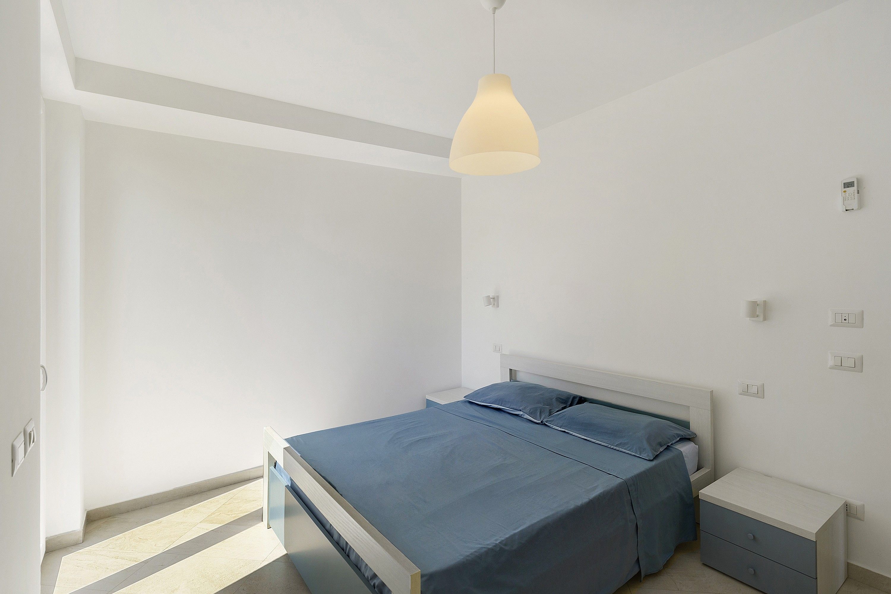 Een slaapkamer met een bed, nachtkastjes, een hanglamp en een deur.
