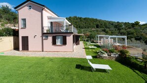 Una casa de dos pisos con un balcón, un patio de piedra y un césped bien cuidado.