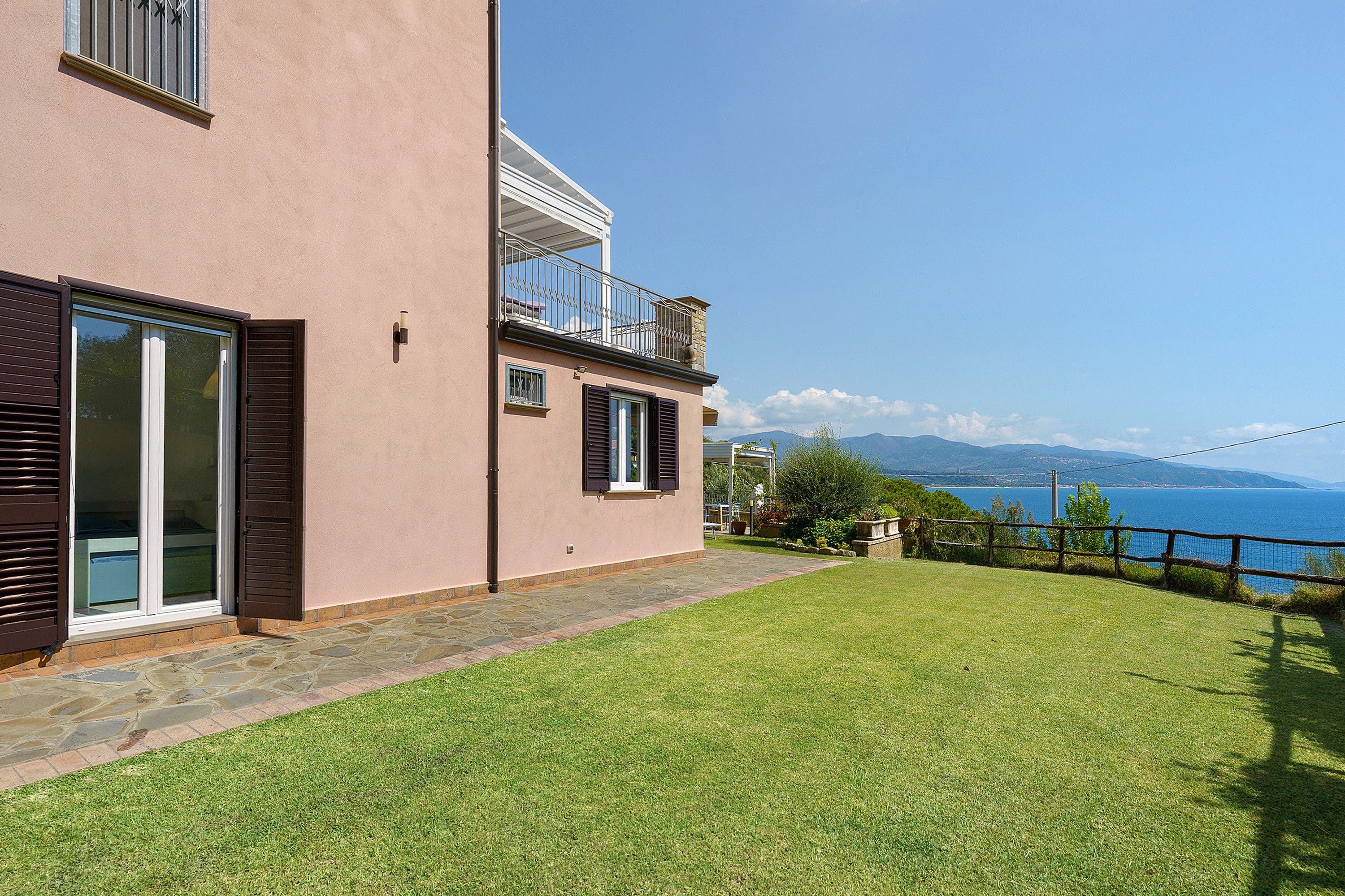 Una casa a due piani con un balcone, un vialetto in pietra e vista sul mare.