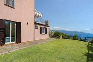 A two-story house with a balcony, a stone pathway, and a view of the sea.