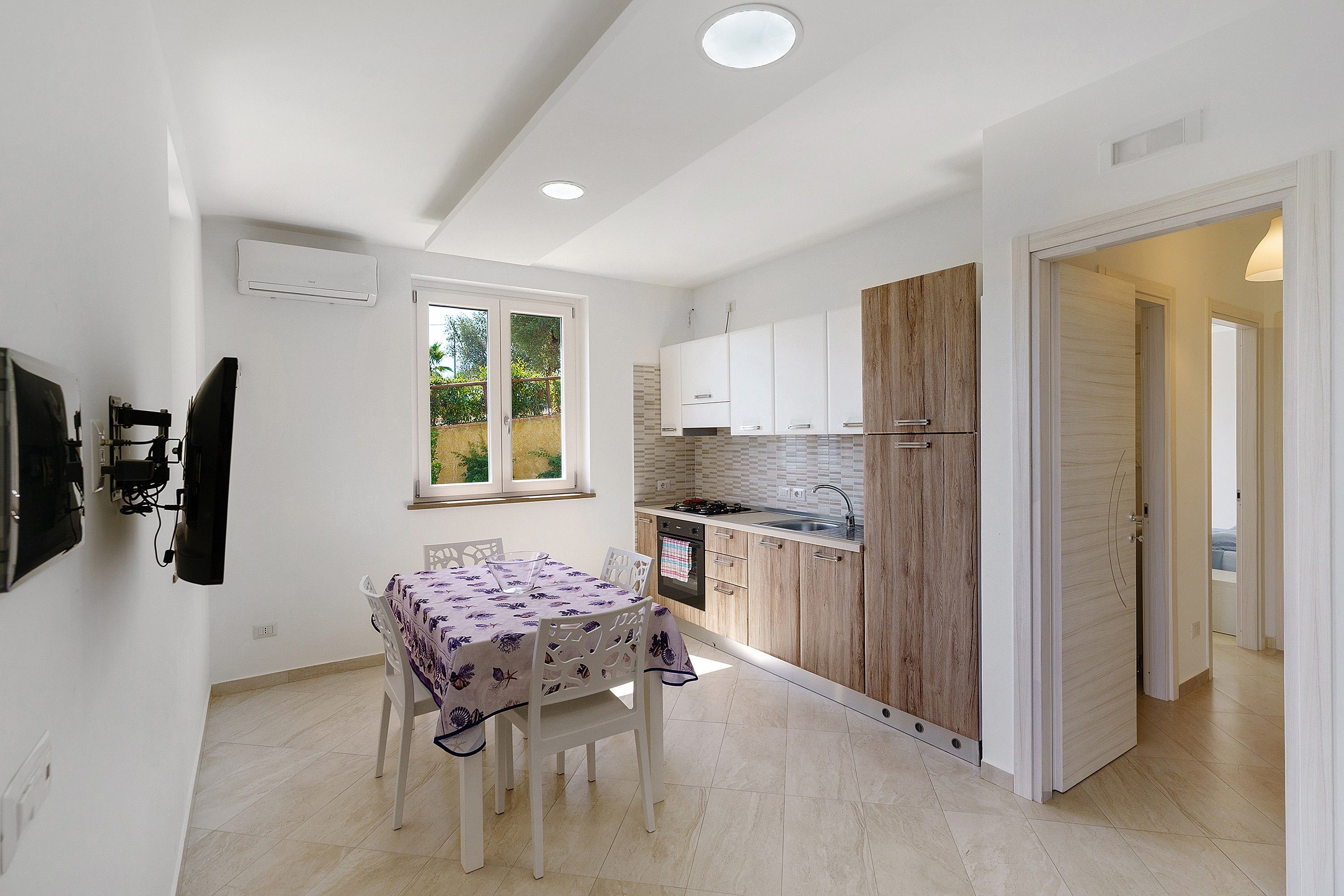 Een compacte keuken met witte kasten, een accentmuur van hout, en een eethoek met een tafel en stoelen.