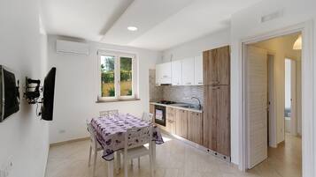 Een compacte keuken met witte kasten, een accentmuur van hout, en een eethoek met een tafel en stoelen.