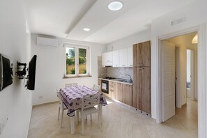 Cocina compacta con armarios blancos, una pared de acento de madera y una zona de comedor con mesa y sillas.