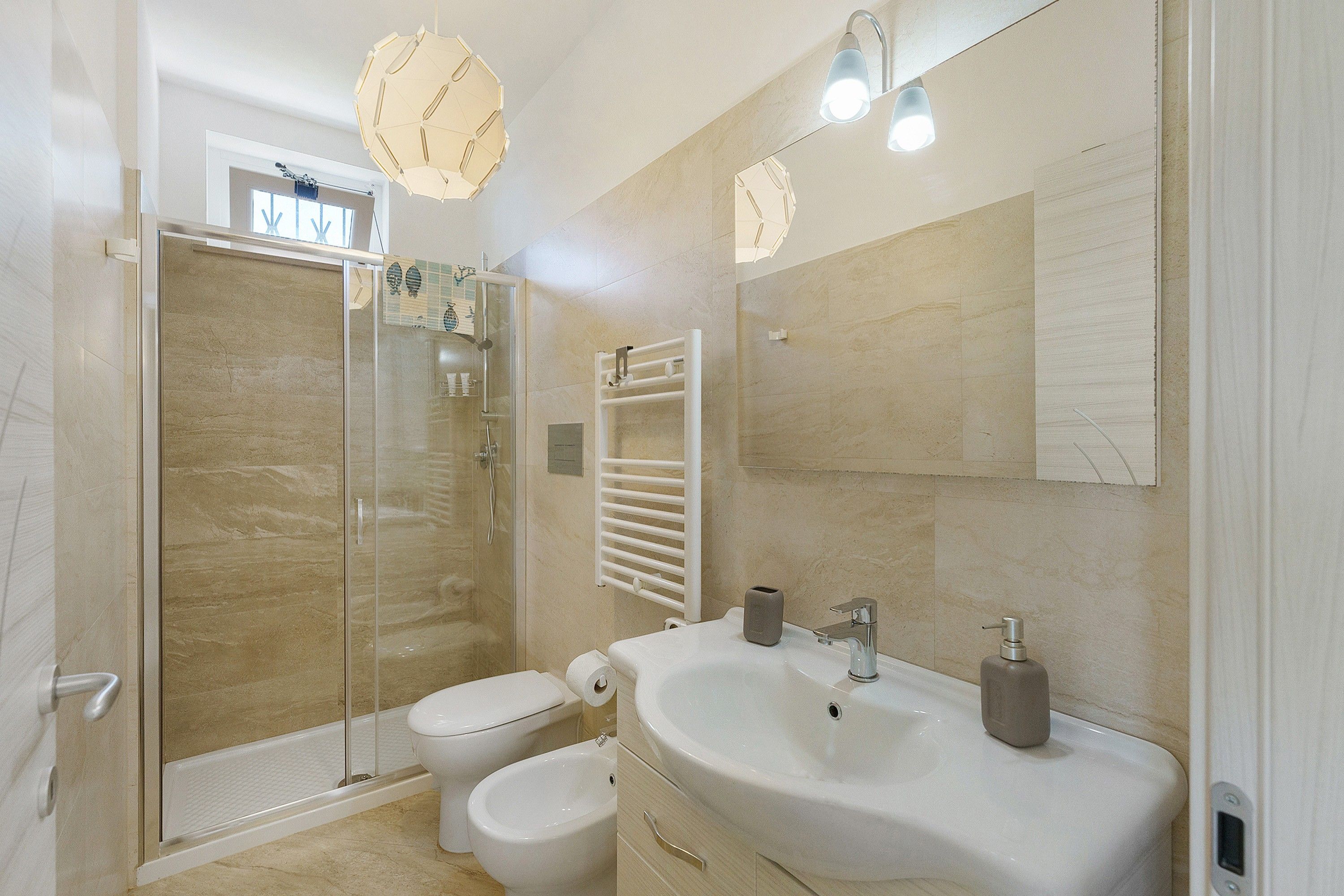 Ein modernes Badezimmer mit einer in Glas eingefassten Dusche, einem weißen Waschbecken mit Seifenspender und einem großen Spiegel.
