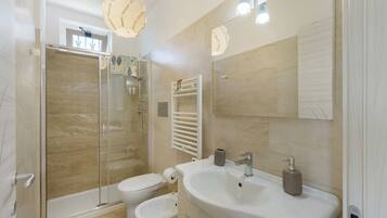 Un bagno moderno con doccia in vetro, un lavandino bianco con dispenser di sapone e uno specchio grande.