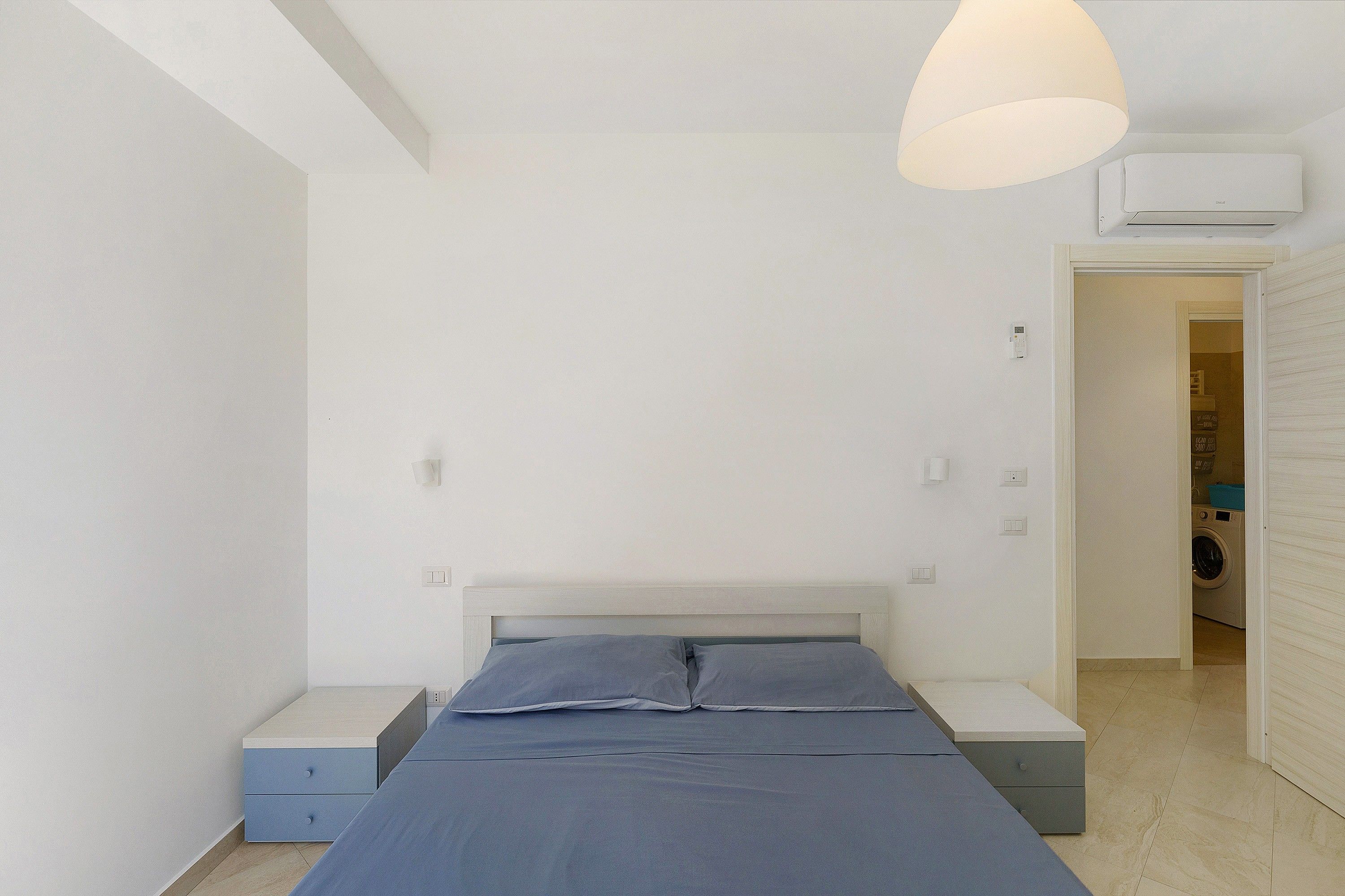 Un dormitorio con cama, mesitas de noche, lámpara colgante y equipo de aire acondicionado.