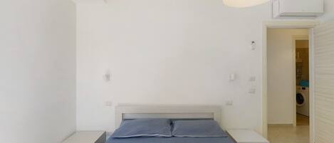 Un dormitorio con cama, mesitas de noche, lámpara colgante y equipo de aire acondicionado.
