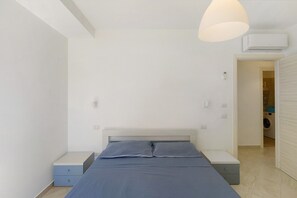 A bedroom with a bed, bedside tables, a hanging light fixture, and an air conditioning unit.