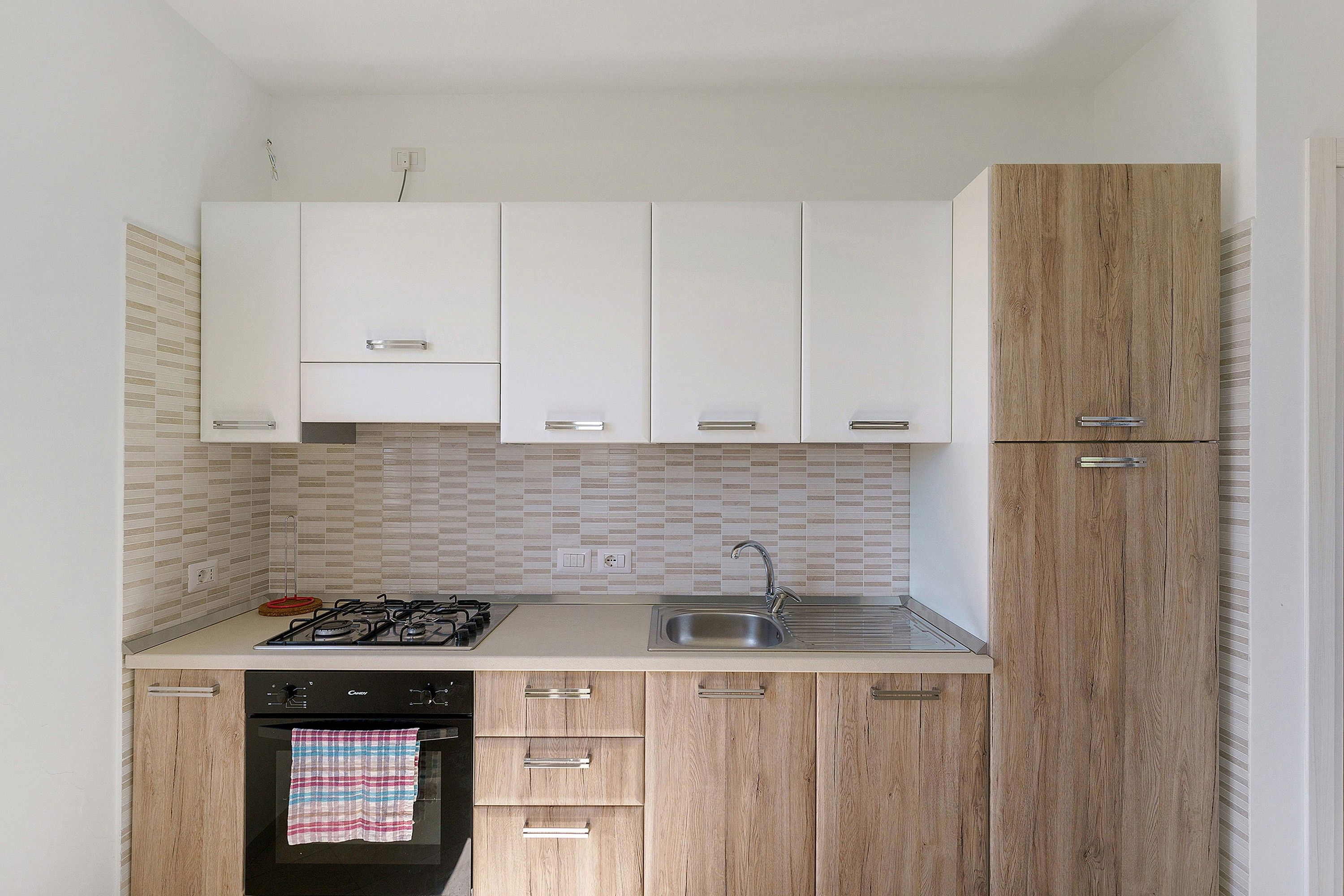 A compact kitchen with white cabinets, a wooden cabinet, a gas stove, a sink, and a tiled backsplash.
